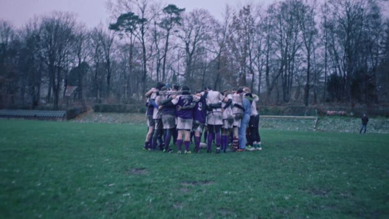 Rugby team huddled together on a grass field before a match.