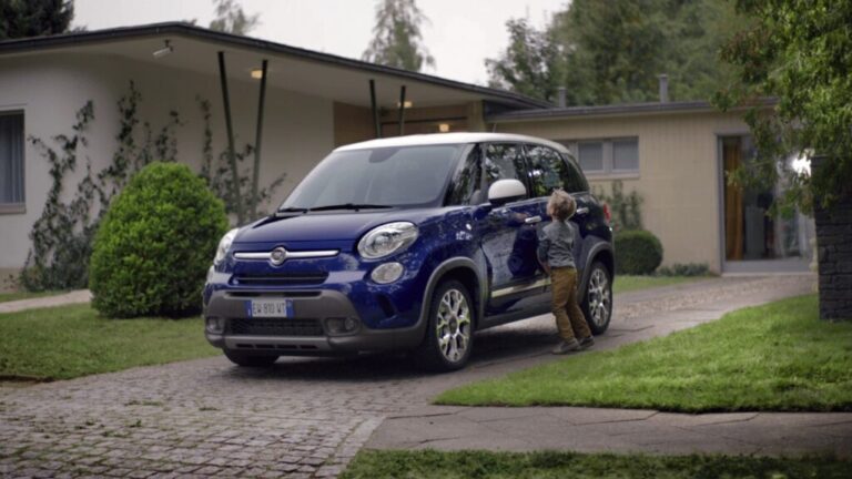 Child touching a blue Fiat parked in a suburban driveway.