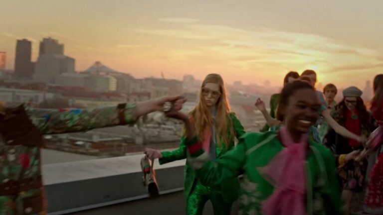 Fashion models dancing on a rooftop at sunset overlooking a city.
