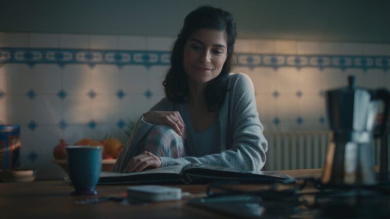 A woman sitting at a kitchen table, reading and smiling softly in a calm home setting.