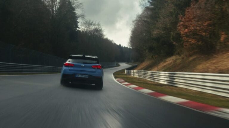 Blue Hyundai driving fast on a winding racetrack surrounded by trees.
