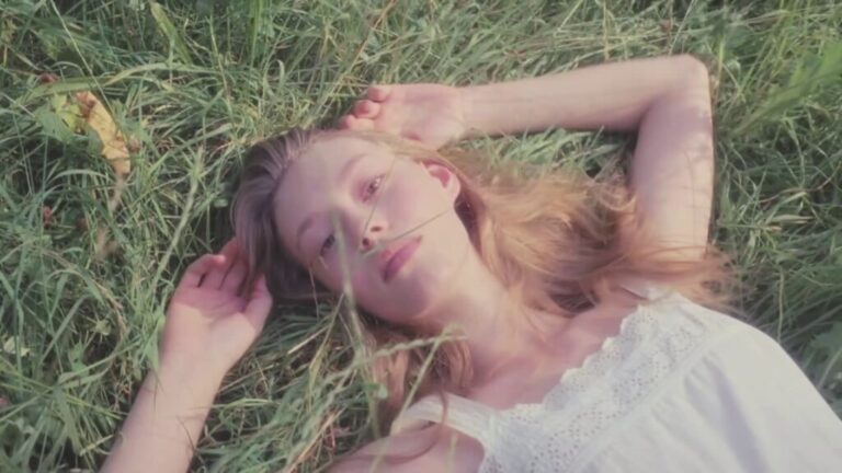 Young woman lying in tall grass, gazing upward in soft natural light.