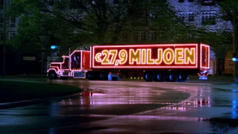 A large truck illuminated with neon lights displaying a monetary amount drives at night on a wet street.