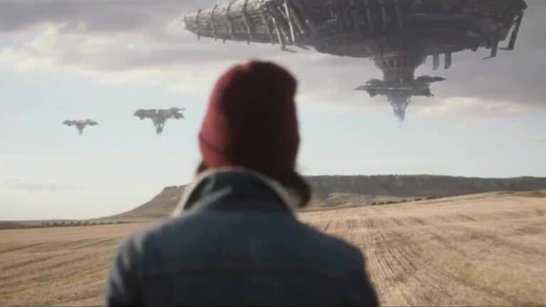 A person stands in an open landscape looking toward large futuristic structures hovering in the sky.