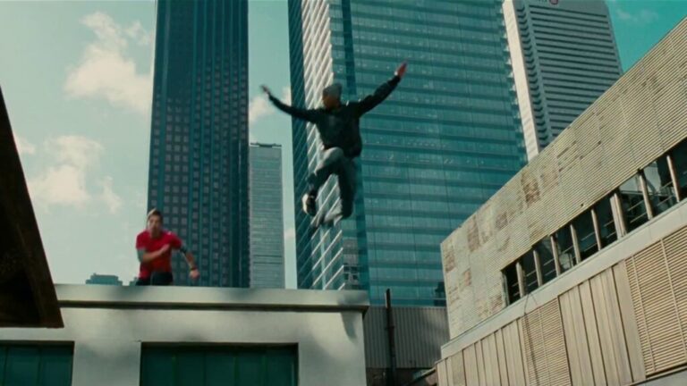 Person mid-air jumping between rooftops in a city.