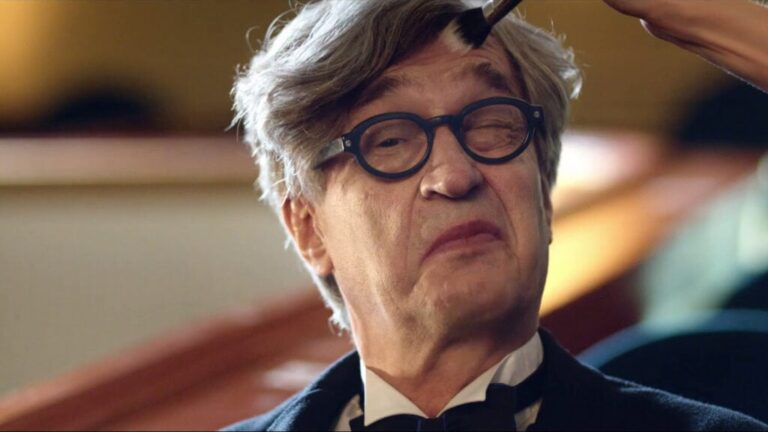 Wim Wenders wearing glasses while having makeup applied.