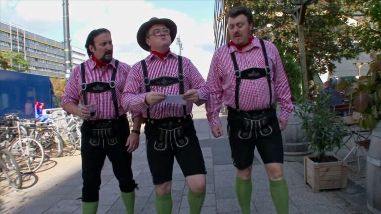 Three men in traditional Bavarian outfits walk together reading a piece of paper.