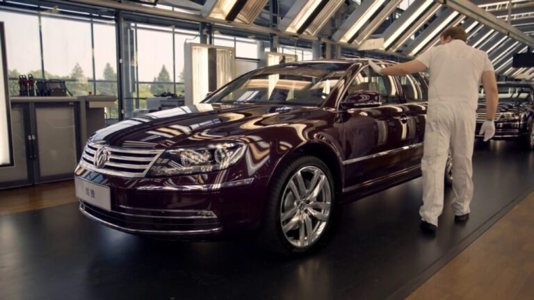 Factory worker inspects a luxury sedan on an assembly line.